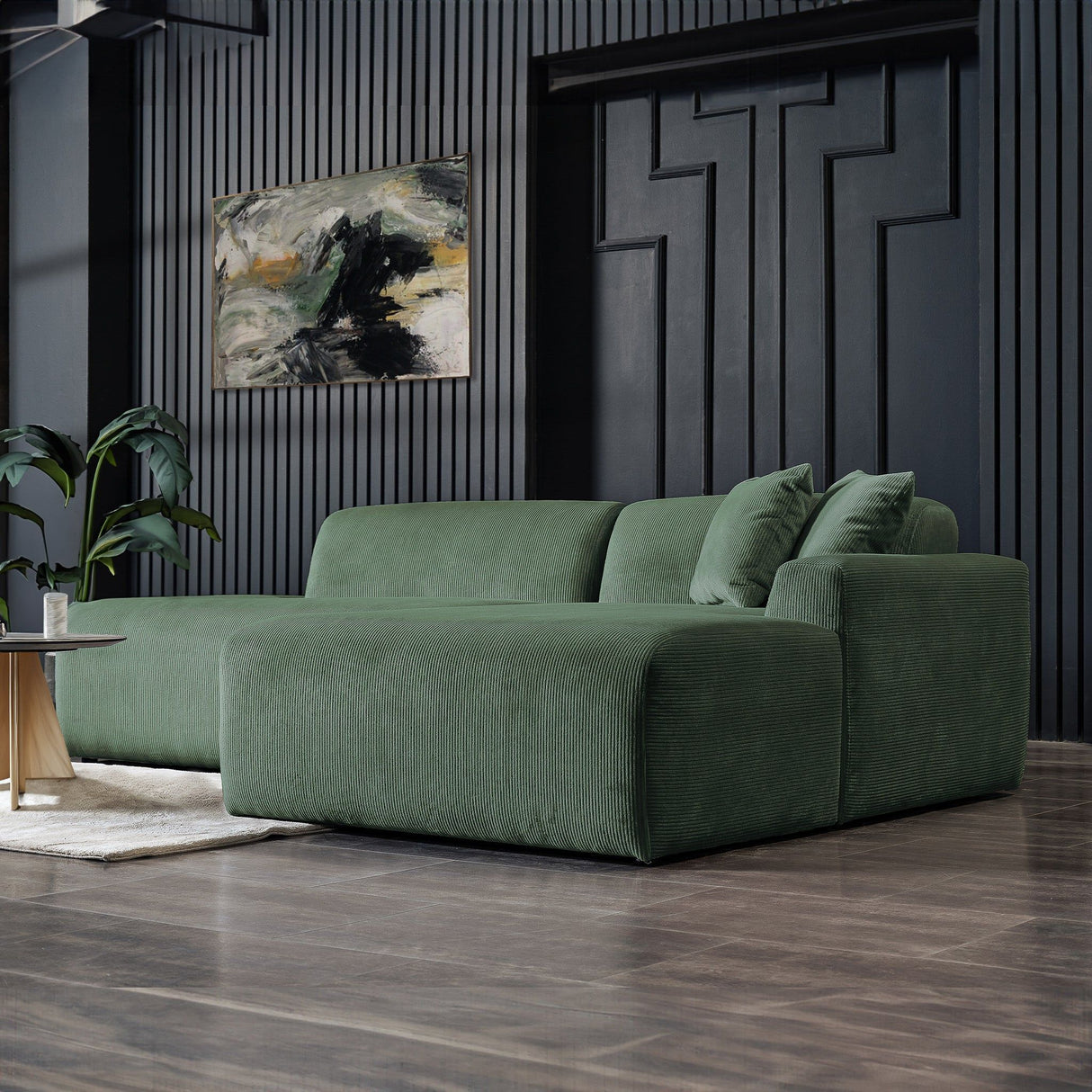 A modern living room features the Mar High-Quality Sectional Sofa in green on polished wooden floors, complemented by a plant and an abstract painting on a dark-textured wall, crafting a stylish and cozy atmosphere.