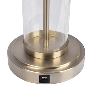 The Luna Table Lamp features a brushed brass base with an integrated USB port. Its clear glass cylinder stem emerges centrally from the base.