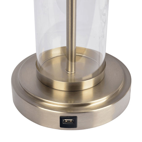 The Luna Table Lamp features a brushed brass base with an integrated USB port. Its clear glass cylinder stem emerges centrally from the base.