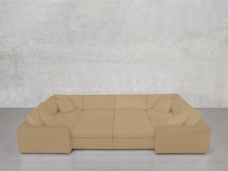 An 8-Seat Modular Closed Pit sectional in beige, featuring wide armrests, a modern design, and four matching throw pillows, sits against a light gray textured wall on a polished concrete floor.