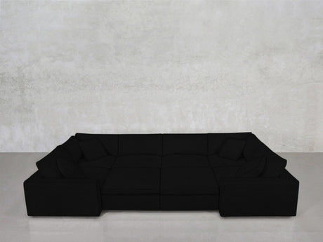 An 8-Seat Modular Closed Pit in black, featuring four matching cushions, sits against a light gray textured wall on a smooth, light floor.