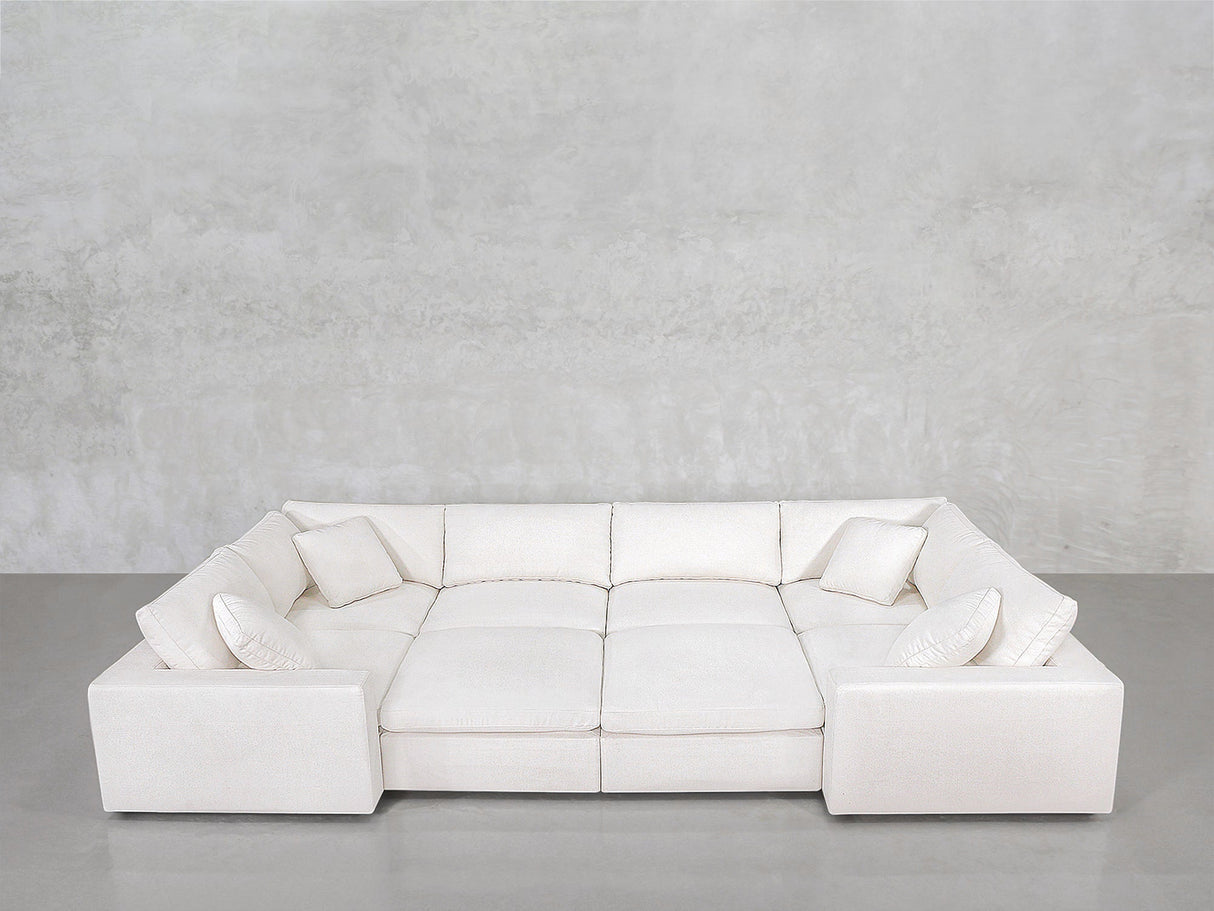 The 8-Seat Modular Closed Pit, a large white U-shaped sectional with six matching throw pillows, is arranged on a gray concrete floor against a light gray textured wall.