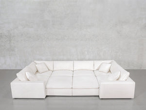 The 8-Seat Modular Closed Pit, a large white U-shaped sectional with six matching throw pillows, is arranged on a gray concrete floor against a light gray textured wall.