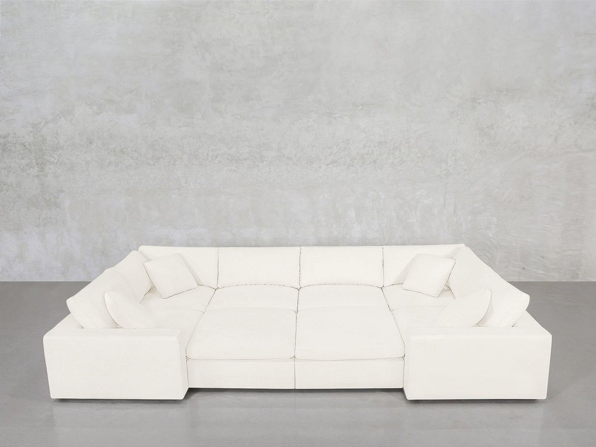 An 8-Seat Modular Closed Pit sectional in modern white, featuring four seat cushions and six matching pillows, is arranged against a light gray concrete wall and a gray floor.
