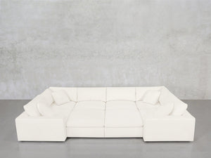 An 8-Seat Modular Closed Pit sectional in modern white, featuring four seat cushions and six matching pillows, is arranged against a light gray concrete wall and a gray floor.