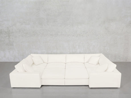 An 8-Seat Modular Closed Pit sectional in modern white, featuring four seat cushions and six matching pillows, is arranged against a light gray concrete wall and a gray floor.