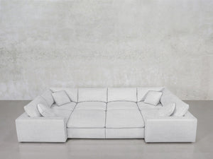 The 8-Seat Modular Closed Pit, a modern light gray sectional with four matching cushions, wide armrests, and a low backrest, is set against a textured light gray wall above a smooth gray floor.