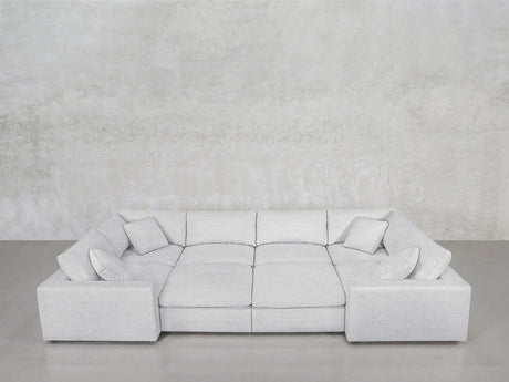 The 8-Seat Modular Closed Pit, a modern light gray sectional with four matching cushions, wide armrests, and a low backrest, is set against a textured light gray wall above a smooth gray floor.