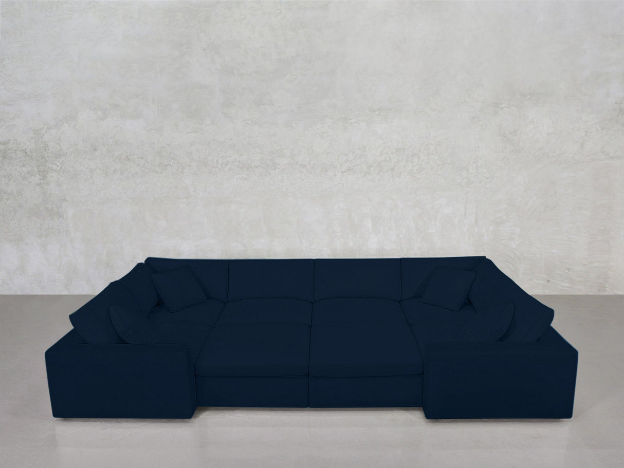An 8-Seat Modular Closed Pit in dark blue with cushions sits against a light gray textured wall on a smooth, light gray floor.