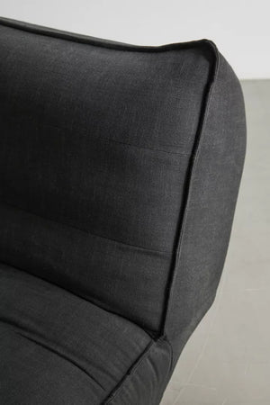 Close-up of the Greta XL Sleeper Sofa in dark gray fabric set against a light gray background. The focus is on the corner of the sofa, highlighting its stitched edges and cushioned backrest.