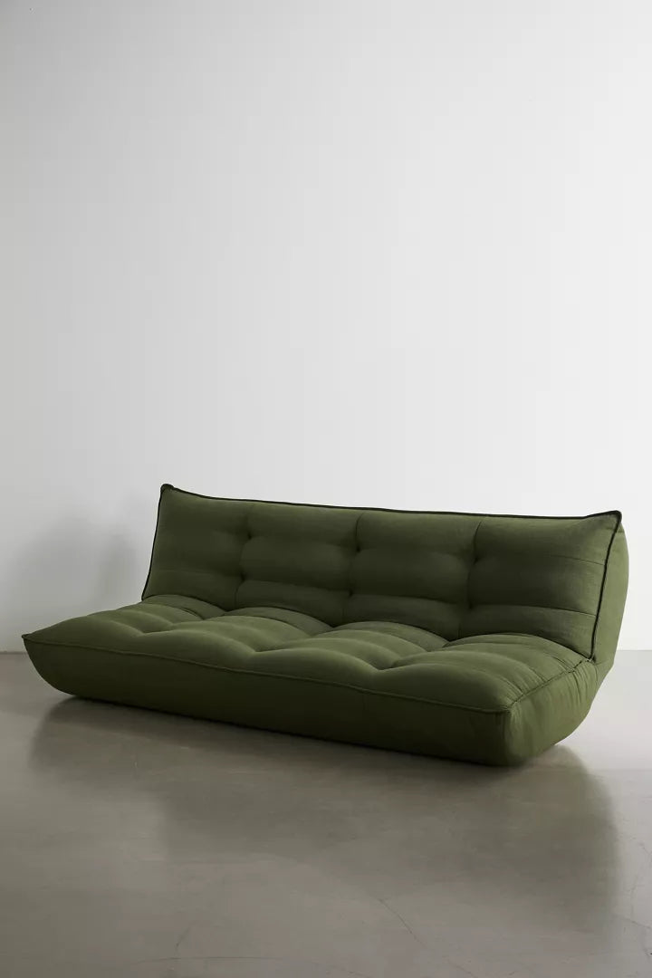 Greta XL Sleeper Sofa in green, featuring a modern low-profile design with tufted cushions, showcased on a polished concrete floor against a plain white wall.
