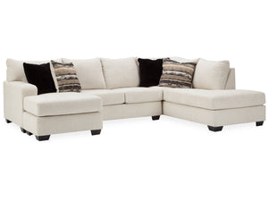 The Cambri 2-Piece Sectional with Chaise features a large beige design with a left chaise and right arm, complemented by three black pillows and two patterned pillows, all set against a white backdrop.
