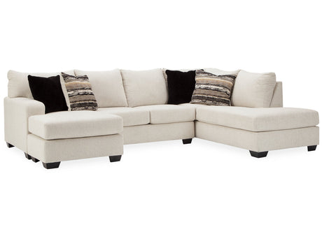 The Cambri 2-Piece Sectional with Chaise features a large beige design with a left chaise and right arm, complemented by three black pillows and two patterned pillows, all set against a white backdrop.