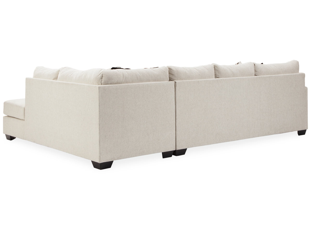 The Cambri 2-Piece Sectional with Chaise, a spacious light beige couch adorned with plush cushions, is set against a white backdrop. Its L-shaped design showcases sleek lines, complemented by short, dark legs visible underneath.
