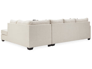 The Cambri 2-Piece Sectional with Chaise, a spacious light beige couch adorned with plush cushions, is set against a white backdrop. Its L-shaped design showcases sleek lines, complemented by short, dark legs visible underneath.