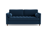 The Briar Sleeper Sofa is a dark blue piece featuring tufted cushions and two round bolster pillows, designed in a modern style with wooden legs that give it a clean, sleek appearance against a black background.