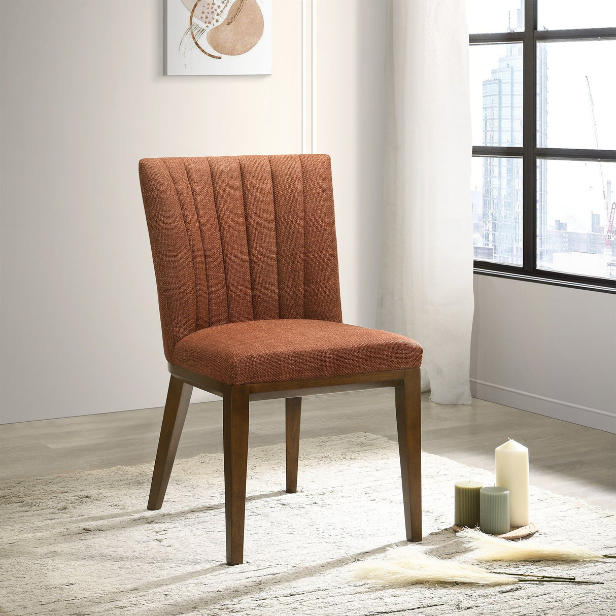 A set of Elmwood - Stylish Dining Chairs with brown upholstery and wooden legs is placed on a light rug in a bright room near a large window showcasing city views, surrounded by candles and a small wall décor piece.