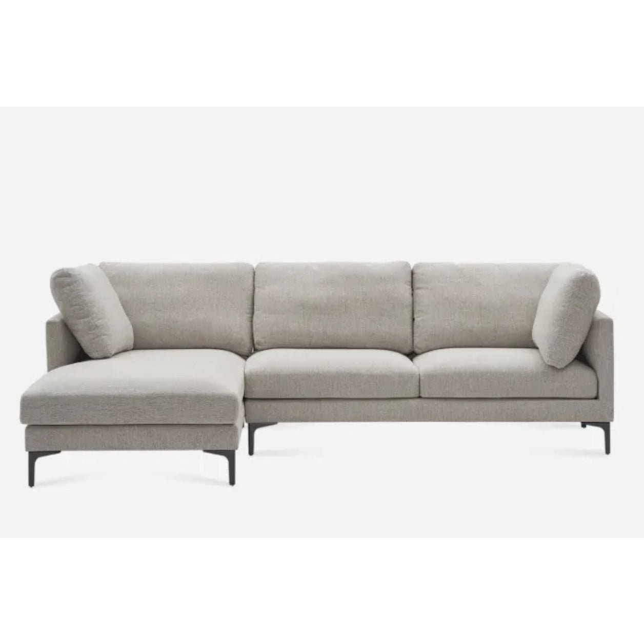 A modern L-shaped sectional sofa with a light gray fabric upholstery. It features three cushions on the backrest, two armrest pillows, and dark, slender legs. The longer chaise section is on the left side.