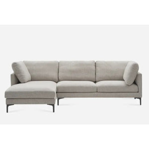 A modern L-shaped sectional sofa with a light gray fabric upholstery. It features three cushions on the backrest, two armrest pillows, and dark, slender legs. The longer chaise section is on the left side.
