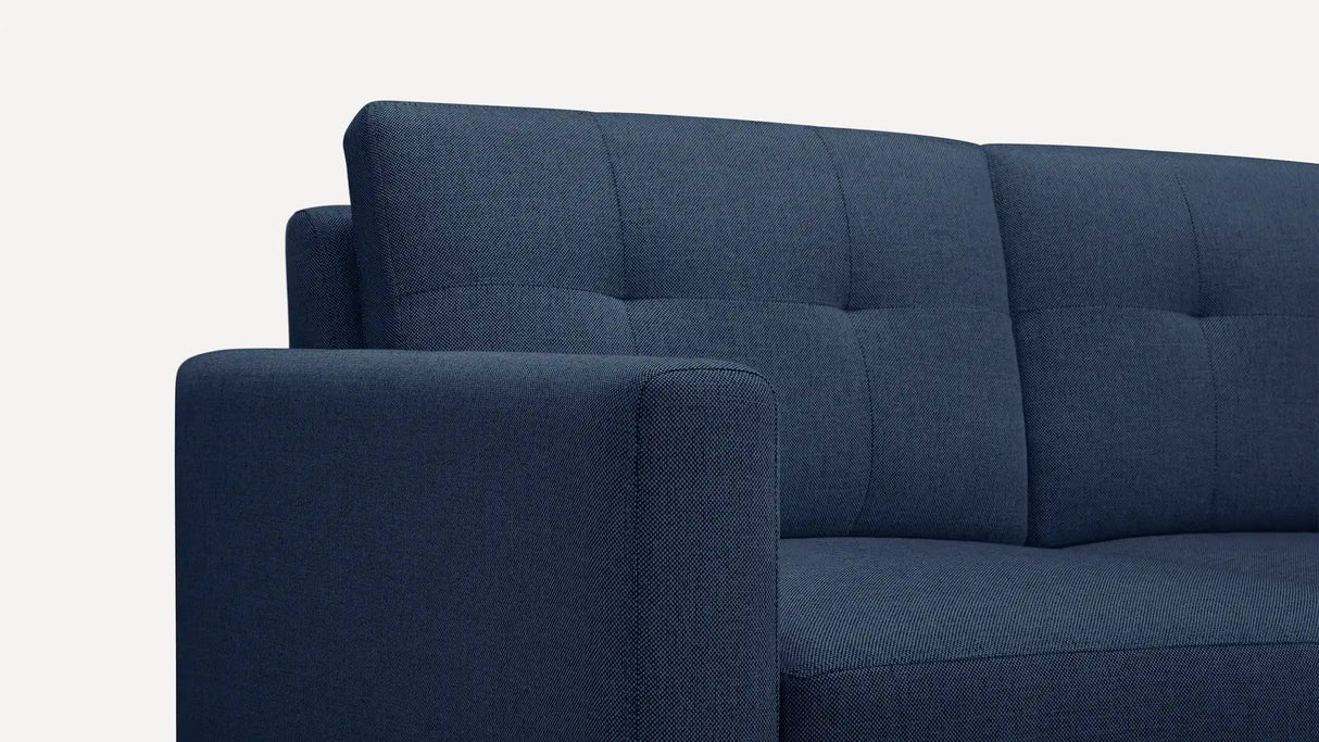 Close-up of the Nomad Fabric Sofa in a dark blue, textured, tufted design set against a pale background. The image emphasizes the sofa's backrest and armrest, showcasing its modern and minimalist style.
