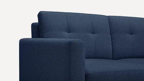 Close-up of the Nomad Fabric Sofa in a dark blue, textured, tufted design set against a pale background. The image emphasizes the sofa's backrest and armrest, showcasing its modern and minimalist style.