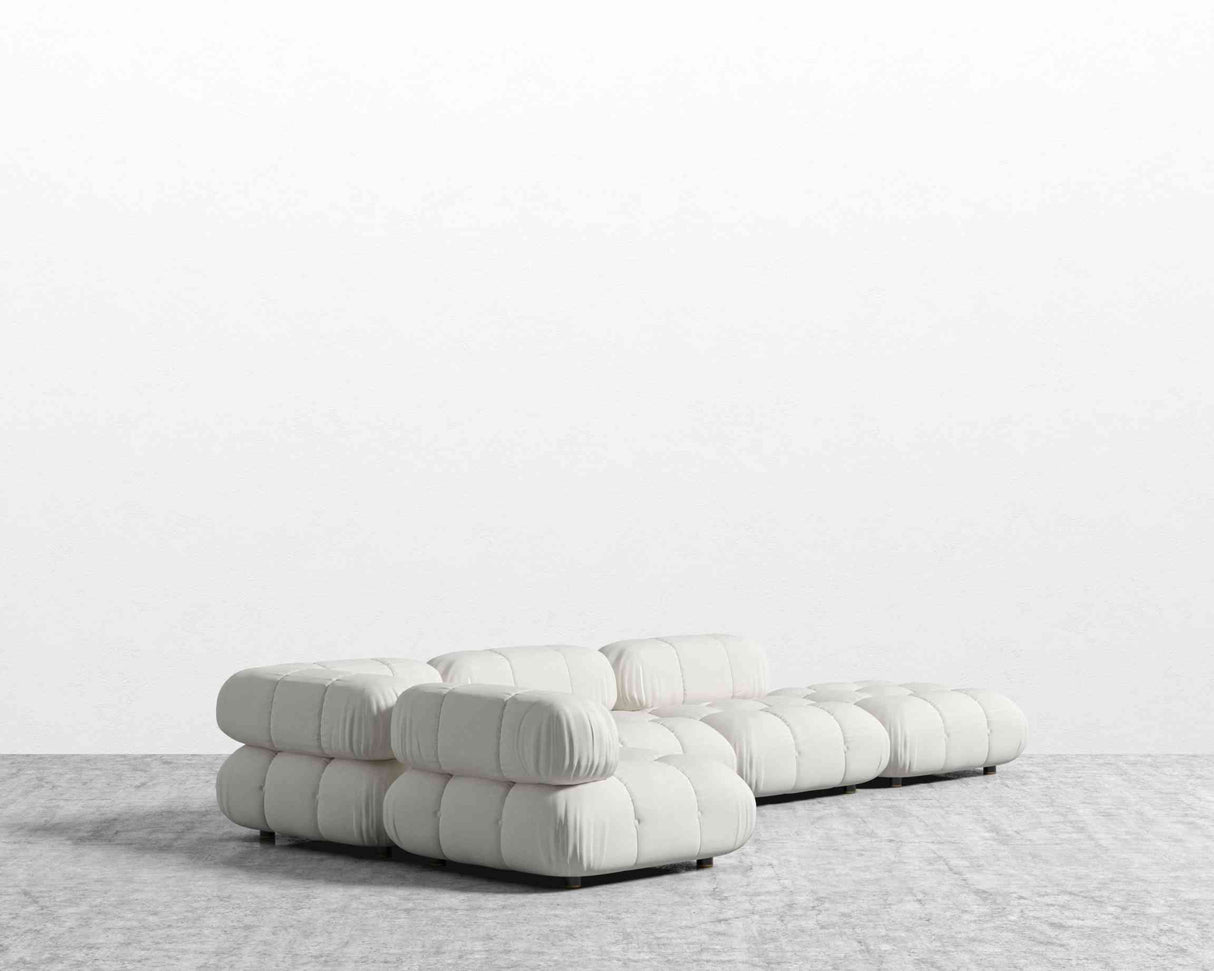 The Belia Modular Sectional, featuring a modern design with rounded cushions in a crisp white finish, rests on a light gray carpet against a plain white wall, establishing a minimalist and contemporary atmosphere.
