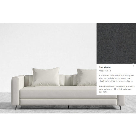 The Berlin Sleeper Sofa is a contemporary piece in a light shade, featuring two large and two smaller cushions. It is upholstered in the "Stockholm Modern Felt" fabric, renowned for its soft and durable qualities. The accompanying image displays a fabric sample with a dark, textured appearance.