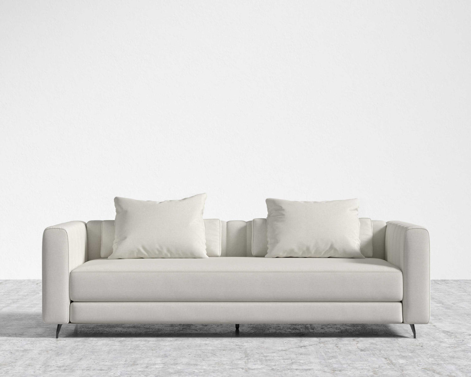 The Berlin Sleeper Sofa, featuring a modern and sleek minimalist design with smooth lines and subtle tufting on the arms, is placed against a plain white wall on a textured gray carpet. This light gray sofa comes with two matching square cushions.