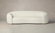 The Chelsea Sofa in Italian Bouclé White, featuring a modern oval shape and plush texture, sits against a plain, neutral-colored background. With its rounded armrests and minimalist design, it offers a sleek and contemporary look.