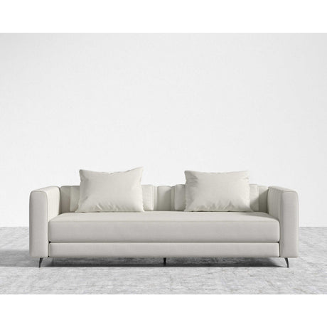 The Berlin Sleeper Sofa, in a sleek light gray, comes with two matching cushions and is positioned on a textured gray area rug against a plain white wall, showcasing its design with clean lines and minimalist aesthetic.
