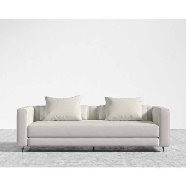 The Berlin Sleeper Sofa, in a sleek light gray, comes with two matching cushions and is positioned on a textured gray area rug against a plain white wall, showcasing its design with clean lines and minimalist aesthetic.