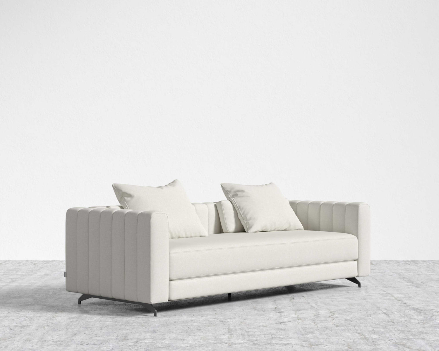 A Berlin Sleeper Sofa, featuring a modern and sleek ribbed design in light gray, sits on a matching light gray carpet. Two complimentary cushions enhance the minimalist and elegant setting against the plain white wall backdrop.