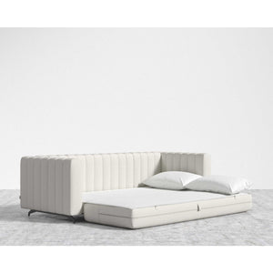 The Berlin Sleeper Sofa, featuring a modern cream color and a ribbed backrest, unfolds into a flat bed. It comes with two white pillows and is set on a light gray carpet against a plain white wall.