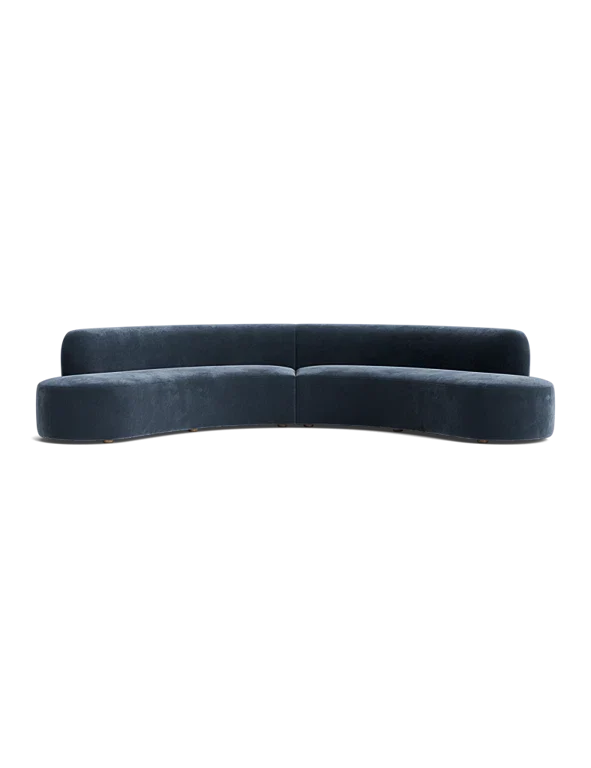 The Cara Sectional Sofa features a curved design in dark blue velvet with no visible legs, set against a black background. It boasts a sleek, minimalist aesthetic with smooth lines and a modern appearance.
