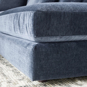 Close-up of the Monterey Modular 3 Piece L Shaped Sectional Sofa in a modern blue-gray fabric with a textured finish, resting on a light-colored, patterned rug. The image highlights the sofa cushions and upholstery details.
