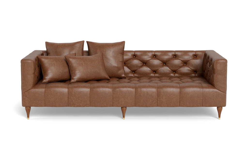 The Ms. Chesterfield Leather Custom Sofa, featuring a classic and elegant design, is upholstered in brown leather with squared arms and back. It stands on wooden legs and is adorned with meticulously arranged matching cushions, including two large and two small ones, enhancing its tufted seating.