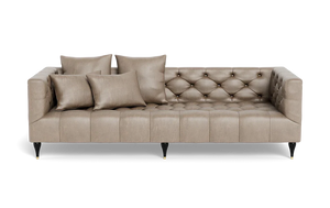 The Ms. Chesterfield Leather Custom Sofa boasts a modern design with its beige tufted finish and plush seating, complemented by sleek black legs with gold accents. This rectangular-shaped sofa comes with four matching cushions, offering both style and comfort for home decor.