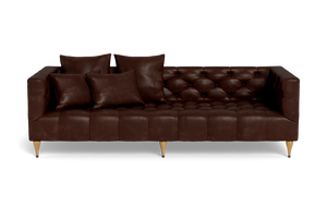 The Ms. Chesterfield Leather Custom Sofa, featuring a luxurious brown leather tufted design and wooden legs, is positioned against a plain background. It is elegantly adorned with four matching cushions, presenting a sleek and modern look.