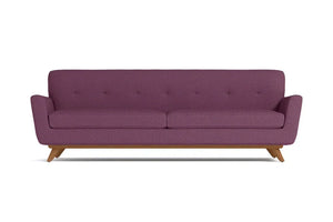 The Carson Sofa is a mid-century modern piece with purple upholstered fabric, featuring a tufted backrest and wooden legs. It boasts a minimalist design and comfortably seats three people.