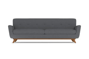 The Carson Sofa offers a modern aesthetic with its dark grey hue and minimalist design. It features a cushioned back adorned with subtle button detailing, sleek armrests, and is supported by mid-century styled wooden legs.