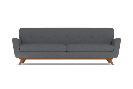 The Carson Sofa offers a modern aesthetic with its dark grey hue and minimalist design. It features a cushioned back adorned with subtle button detailing, sleek armrests, and is supported by mid-century styled wooden legs.