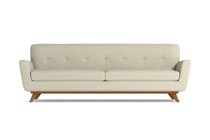 The Carson Sofa is a mid-century modern design featuring a beige color with a tufted backrest and two seat cushions. It is supported by a wooden base and angled legs, all presented against a plain white background.