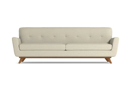 The Carson Sofa is a mid-century modern design featuring a beige color with a tufted backrest and two seat cushions. It is supported by a wooden base and angled legs, all presented against a plain white background.