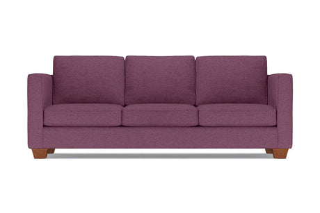 The Catalina Sofa, a plum-colored three-seater with wide armrests and wooden legs, is set against a plain white background. It features three plush seat and back cushions.