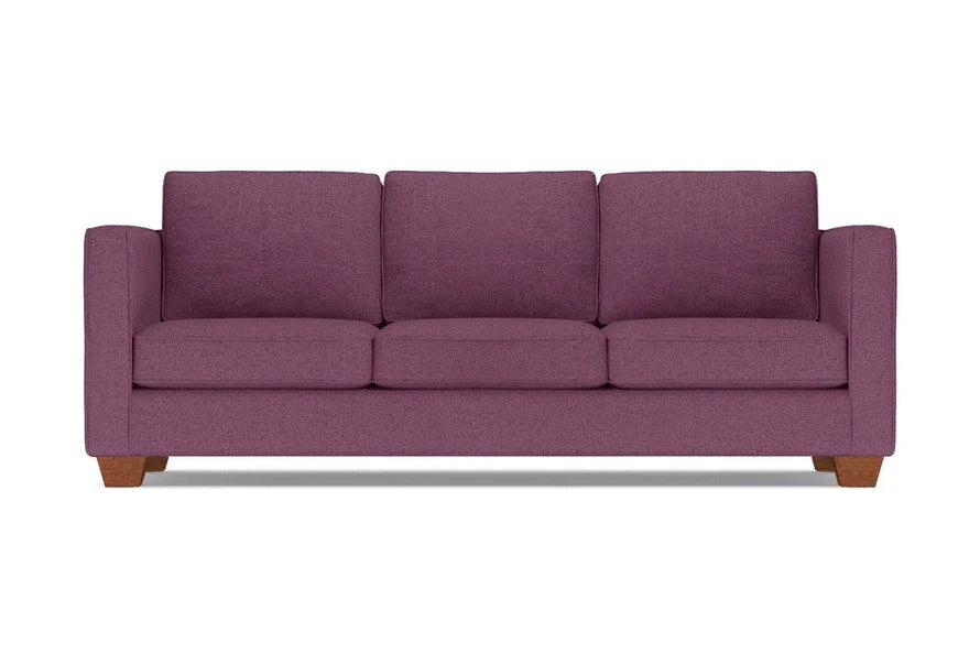 The Catalina Sofa, a plum-colored three-seater with wide armrests and wooden legs, is set against a plain white background. It features three plush seat and back cushions.