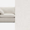 A modern beige sofa with a single cushion is partially visible, extending into a seamless background of the same color and texture, creating a blended and minimalist appearance.