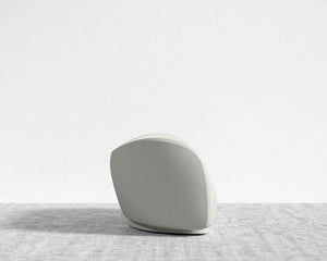 The Diane Sofa, featuring a minimalist design with soft, curved lines in a light gray fabric, rests on a textured light gray rug against a plain white background. The sofa faces away from the viewer, showcasing its simple and modern aesthetic.