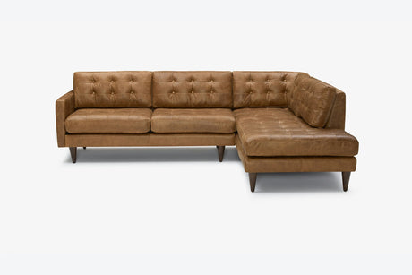 The Eliot Leather Sectional with Bumper, featuring tufted cushions and wooden legs in a brown leather finish, set against a plain white background.