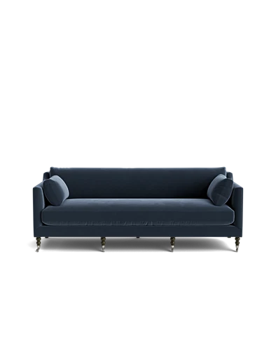 The Fabienne Sofa is a blue, mid-century modern piece featuring cylindrical cushions on each side and spindle legs. It stands out against a plain black background, which highlights its sleek design.