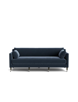 The Fabienne Sofa is a blue, mid-century modern piece featuring cylindrical cushions on each side and spindle legs. It stands out against a plain black background, which highlights its sleek design.